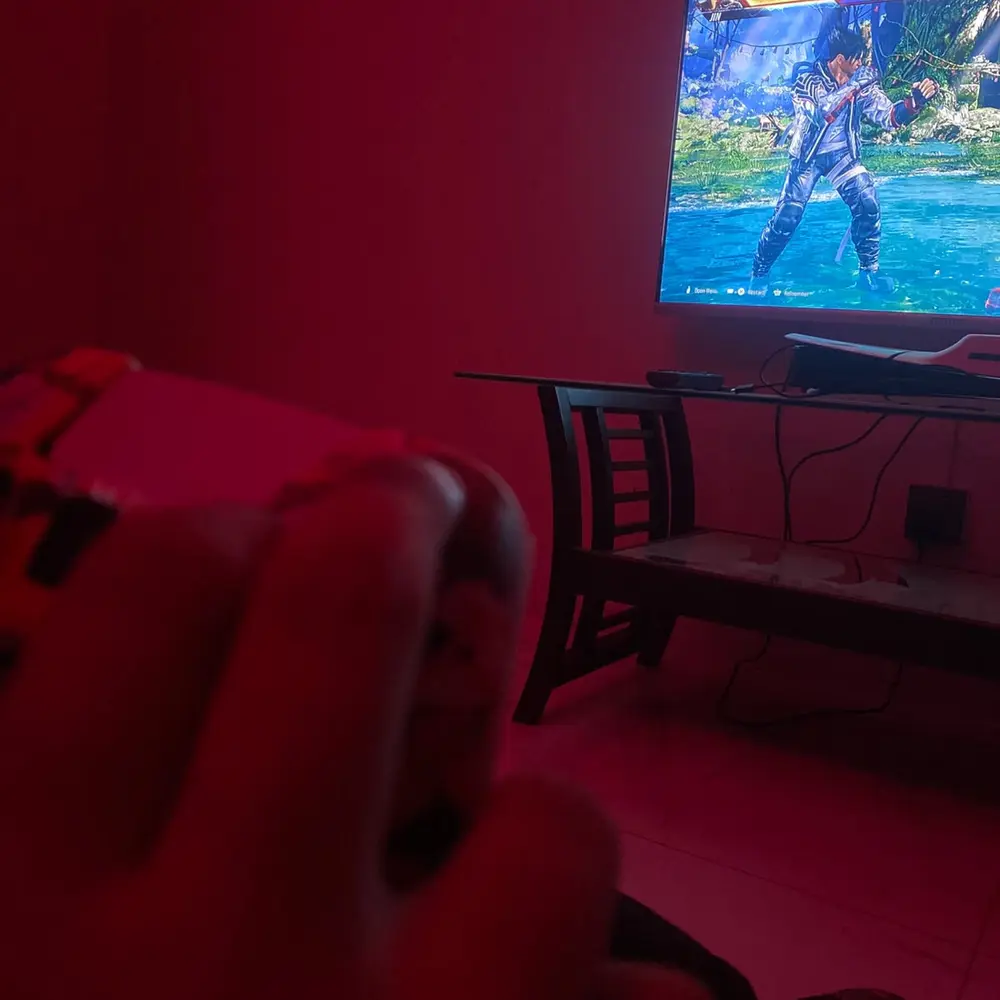 A hand on a DualSense controller in front of a Tekken 8 match